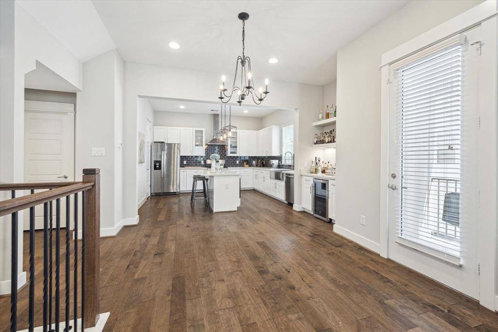 This photo showcases the spacious, open-concept kitchen and dining area with hardwood floors, featuring white cabinetry, stainless steel appliances, and a central island with bar seating.