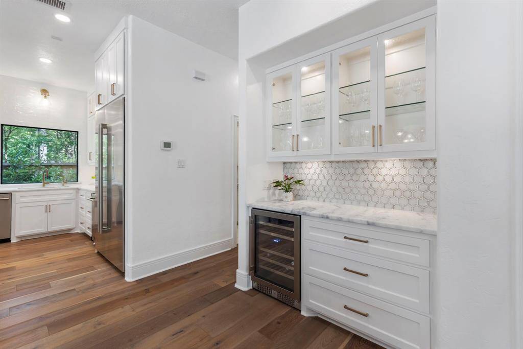 The butler's pantry accented with glass foil tile backsplash, quartzite counters and stunning glass front cabinets. With a dual-temperature wine fridge, this space is ideal for entertaining!