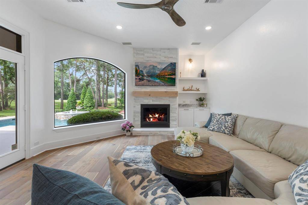 The kitchen opens into a light-filled family room with soaring ceilings, a modern Anthology ceiling fan, and a striking fireplace with floor to ceiling stacked marble stone.