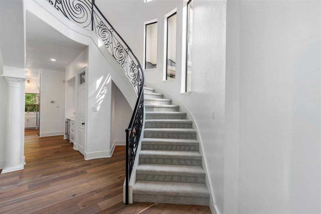 The winding staircase serves as a central focal point of the home, featuring a graceful curve and modern wrought iron railing that adds a touch of architectural elegance. Accented windows along the stairwell bathe the space in natural light, enhancing the staircase's dramatic presence.