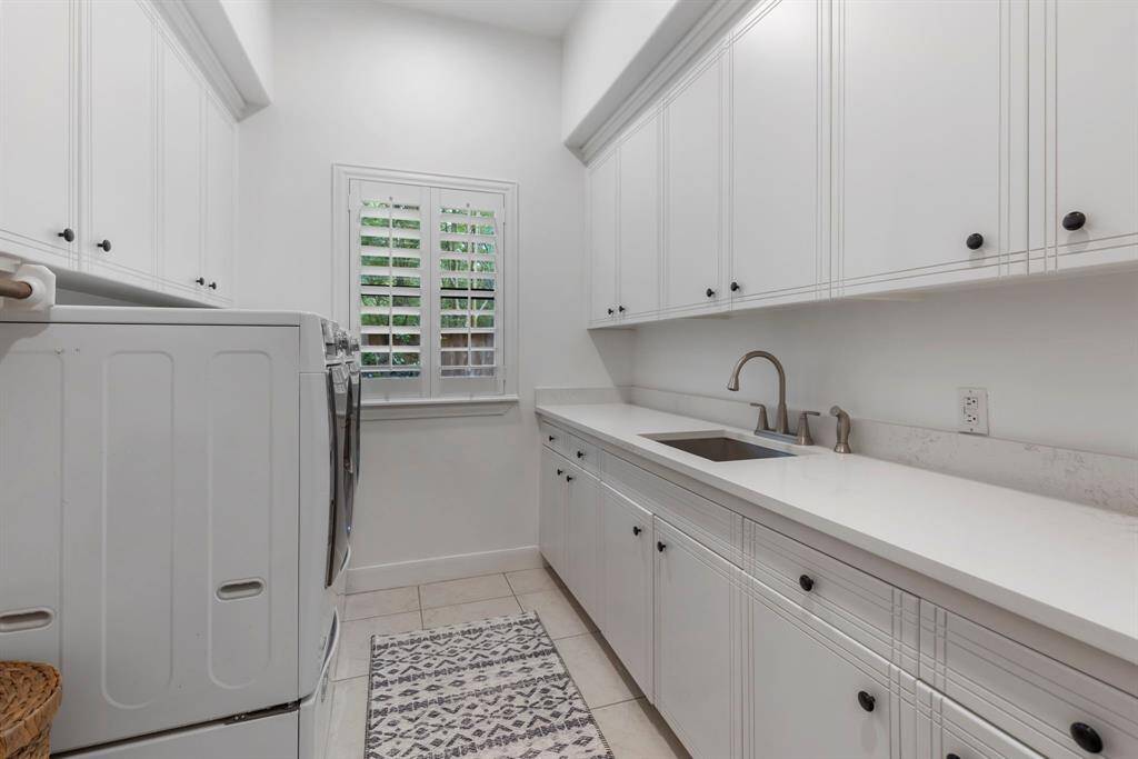 The spacious laundry room is both functional and beautifully designed, featuring an abundance of custom cabinetry and extensive quartz countertops that provide ample space for folding and organization. A built-in sink adds convenience, while durable tile flooring ensures easy maintenance. The room also includes dedicated hanging space for air-drying garments and is wired for surround sound, making laundry a more enjoyable task in this well-appointed space.