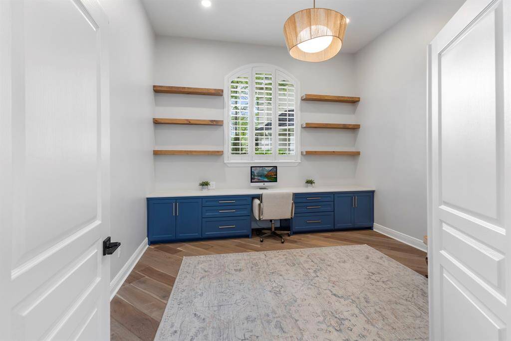 Just off the entry, the private study offers a spacious retreat for work or relaxation, featuring custom built-in cabinetry, a dedicated desk area, stylish floating wood shelving, and plantation shutters on a beautifully curved window.
