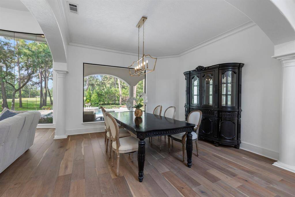 The living area flows seamlessly into the formal dining room, where another picturesque window and a sleek, modern gold-accented designer light fixture create a sophisticated and inviting ambiance.