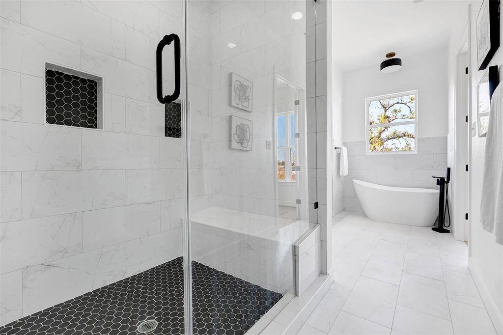 Relax and unwind in this stunning primary bath, complete with a glass-enclosed shower, a luxurious bathtub, and double sinks for added convenience. (Model unit at 1234 E 23rd St. Design and finishes may vary)