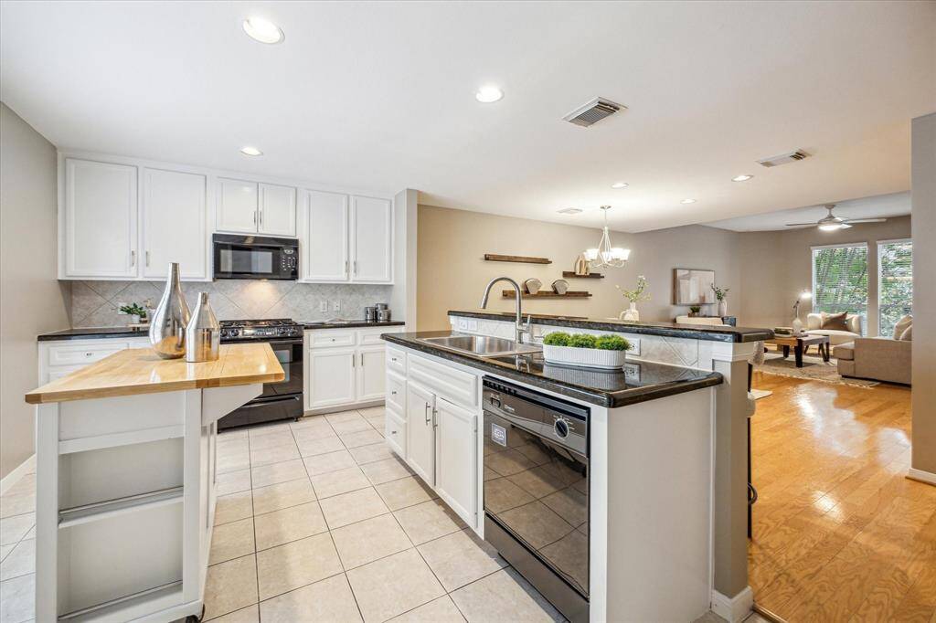 Show off your culinary skills in this beautifully appointed kitchen with crisp white cabinetry, sleek granite countertops, stylish tile backsplash, and black appliances. A raised breakfast bar provides casual seating and opens to the dining and living areas, creating the perfect setup for easy entertaining.
