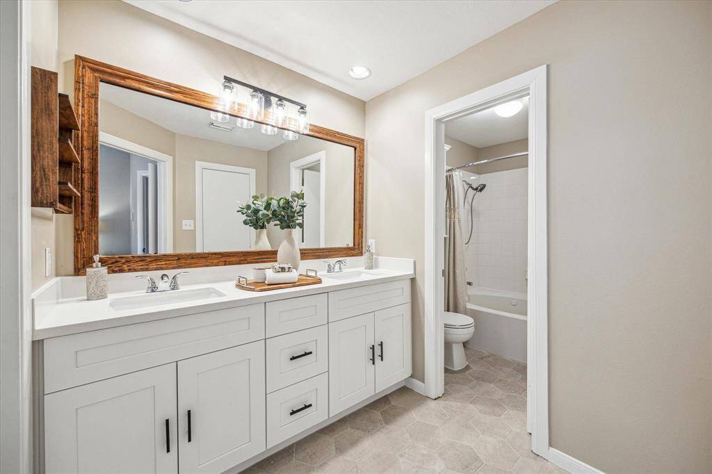 The spa-inspired primary ensuite features a sleek dual sink vanity with ample storage, framed mirror with modern lighting, and stylish tile flooring. A private water closet includes a jetted tub/shower combo, perfect for relaxing at the end of the day.