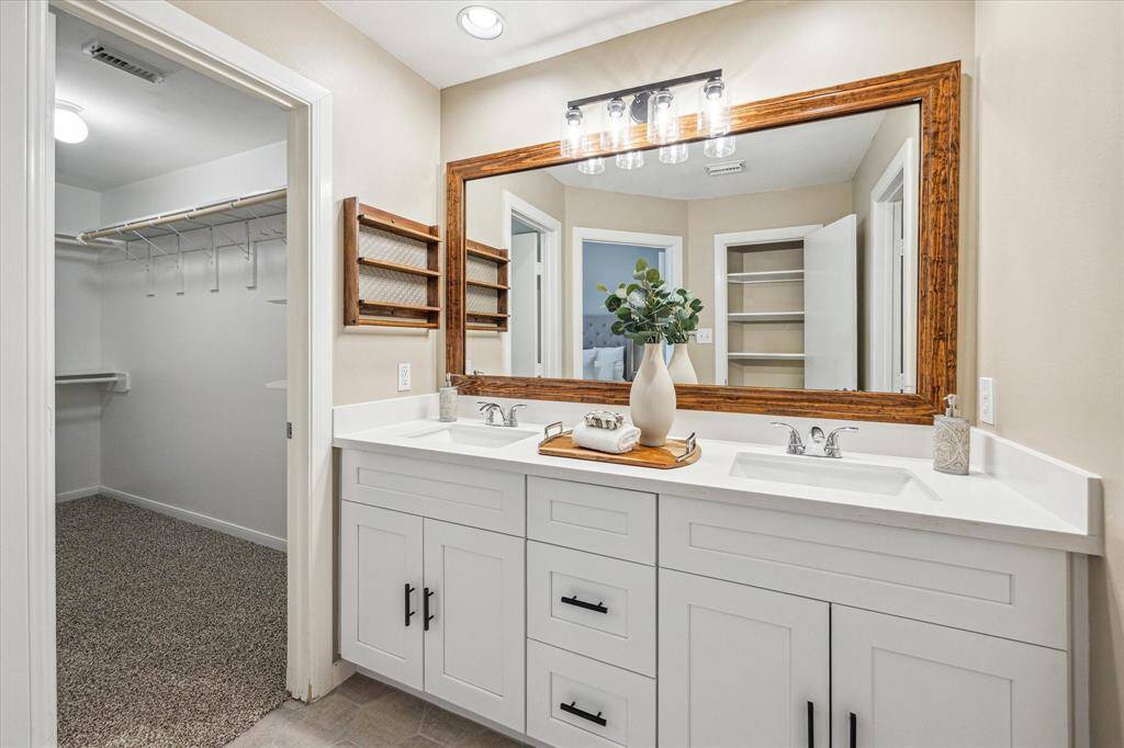 The primary ensuite features a stylish dual sink vanity with sleek countertops, ample drawer and cabinet storage, and a beautifully framed mirror with updated vanity lighting.