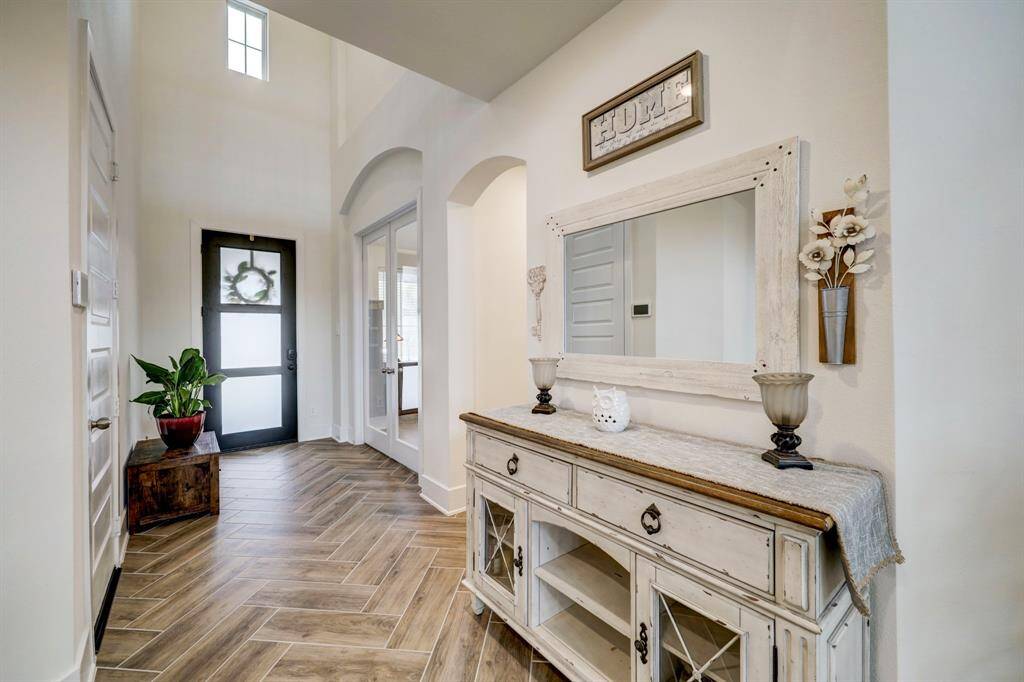 This entryway features high ceilings and a bright, welcoming atmosphere. It includes a stylish herringbone-patterned wood floor, and a modern glass-paneled front door, enhancing the overall charm and functionality.