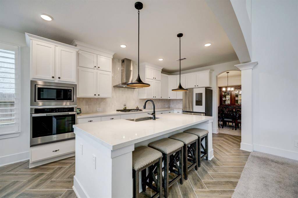 Experience this sleek kitchen with white cabinetry, stainless steel appliances, and a spacious quartz island. Pendant lighting highlights the open layout, seamlessly connecting to the dining area through an elegant arched doorway.