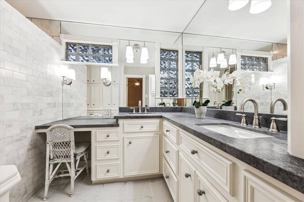 This updated bathroom showcases recently installed tile flooring, dual stainless steel sinks, a spacious vanity area, and a large, modern shower, combining style and functionality.