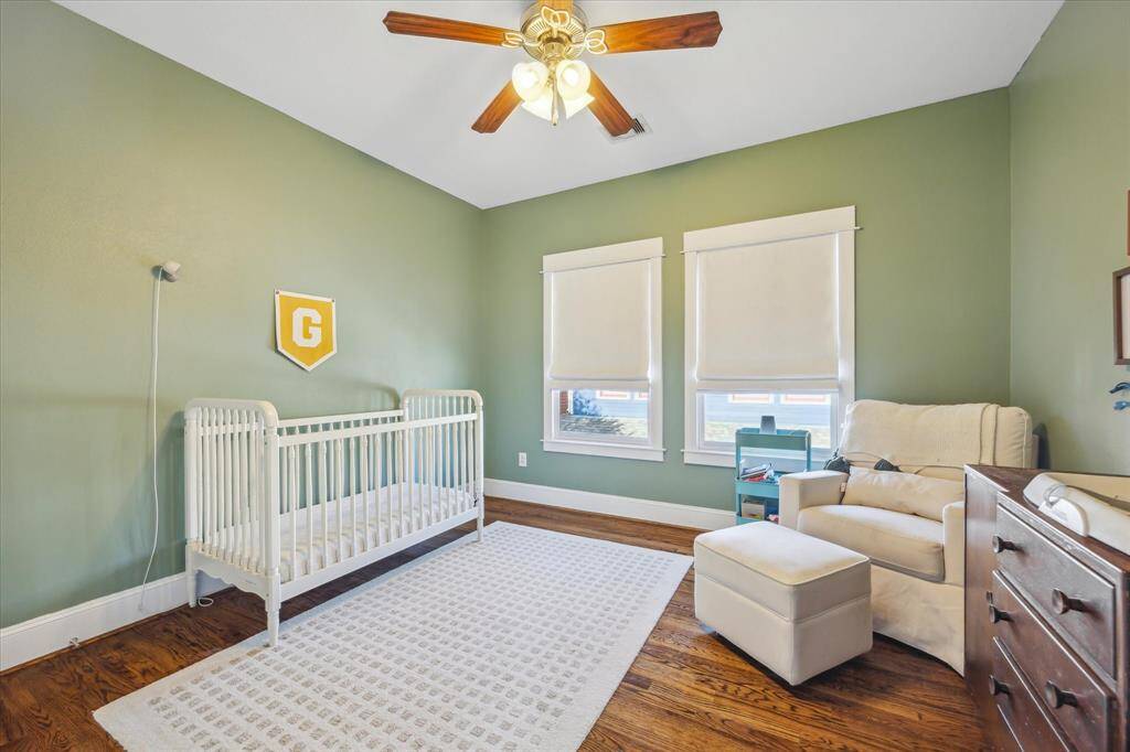 Secondary bedroom, currently a nursery, with ceiling fan, hardwood floors and custom window coverings.