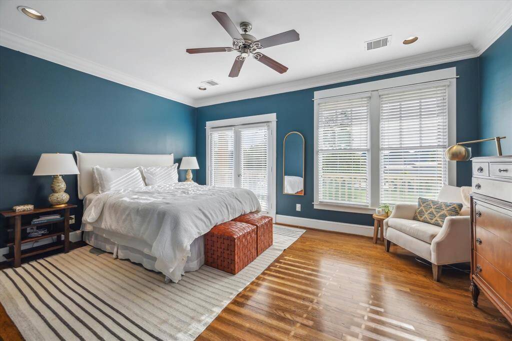 The serene primary suit opens to the front balcony through the French doors. Note the ceiling fan, hardwood floors, and sophisticated crown molding.