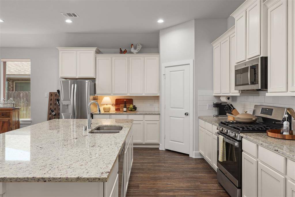 This kitchen features modern white cabinetry, stainless steel appliances, and a large island with granite countertops.