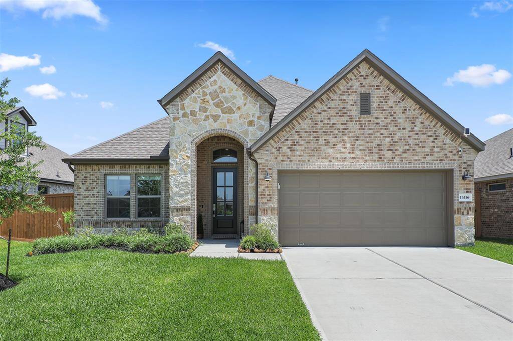 Features a well-maintained lawn, a spacious driveway leading to a two-car garage, and a welcoming arched entryway.
