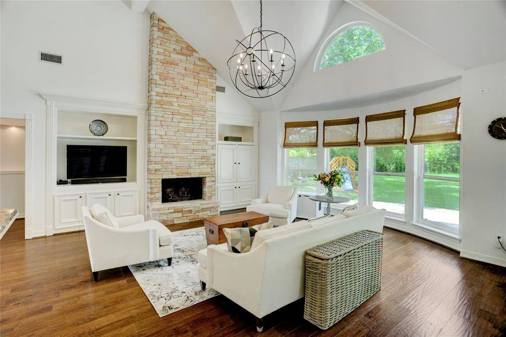 This inviting space features custom shade coverings on expansive windows and elegant built-in cabinets flanking a stunning floor-to-ceiling stone fireplace.