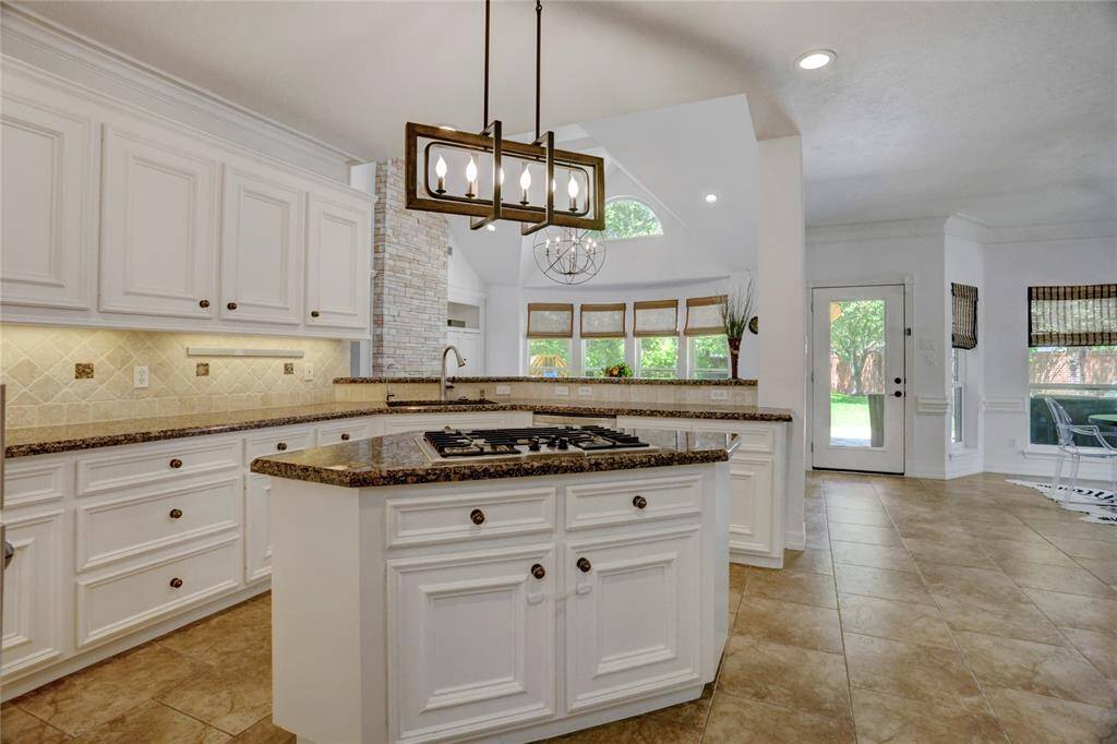 This kitchen boasts a center island with a sleek gas cooktop, ample cabinetry, and elegant lighting, perfect for culinary enthusiasts.