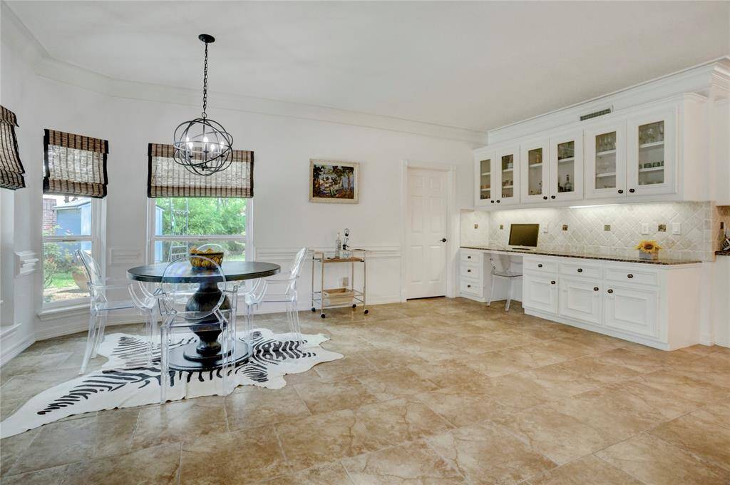 Bright and spacious breakfast dining area with elegant tile flooring and abundant natural light. Features a built-in desk, glass-front cabinets, and contemporary lighting. Ideal for both dining and home office needs.