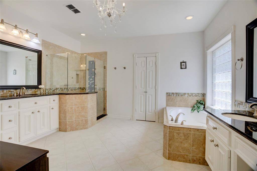 Elegant bathroom featuring a spacious walk-in shower, soaking tub, and dual sinks with granite countertops. Enjoy the bright, airy feel with a chandelier and abundant natural light. Double doors lead to a large walk-in closet with built-in cabinets.