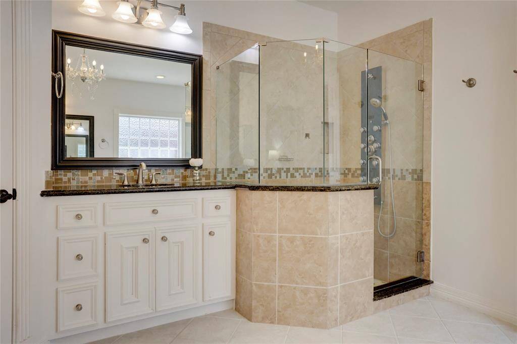 A closer look of the modern glass-enclosed shower with stylish tile accents, a sleek vanity with a dark countertop and contemporary fixtures, and bright lighting that enhances the space's clean, sophisticated look.