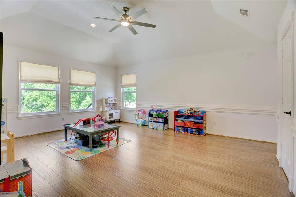 This spacious upstairs game room features elegant, engineered hardwood floors, high ceilings with a fan, and abundant natural light from three large windows with Roman shades. Currently a playroom, it offers versatile potential for your needs.