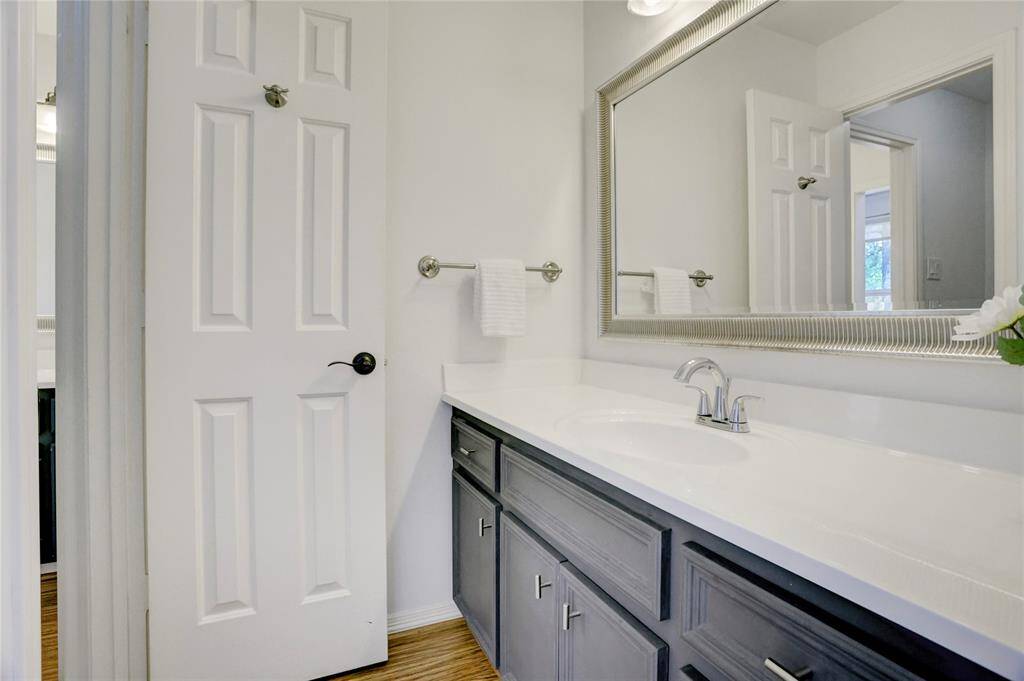 This modern Hollywood bathroom boasts a sleek vanity, spacious countertop, large, framed mirror, and elegant fixtures in a neutral palette. It adjoins a secondary bedroom with a full-length shower and commode in between, offering both style and functionality.