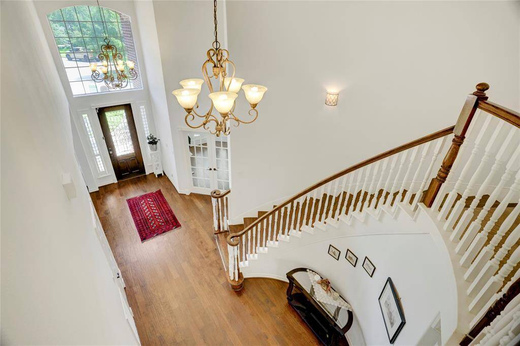 This photo showcases an elegant foyer with a high ceiling, large windows, and a grand staircase. The space features hardwood floors, a decorative chandelier, and a welcoming entrance.