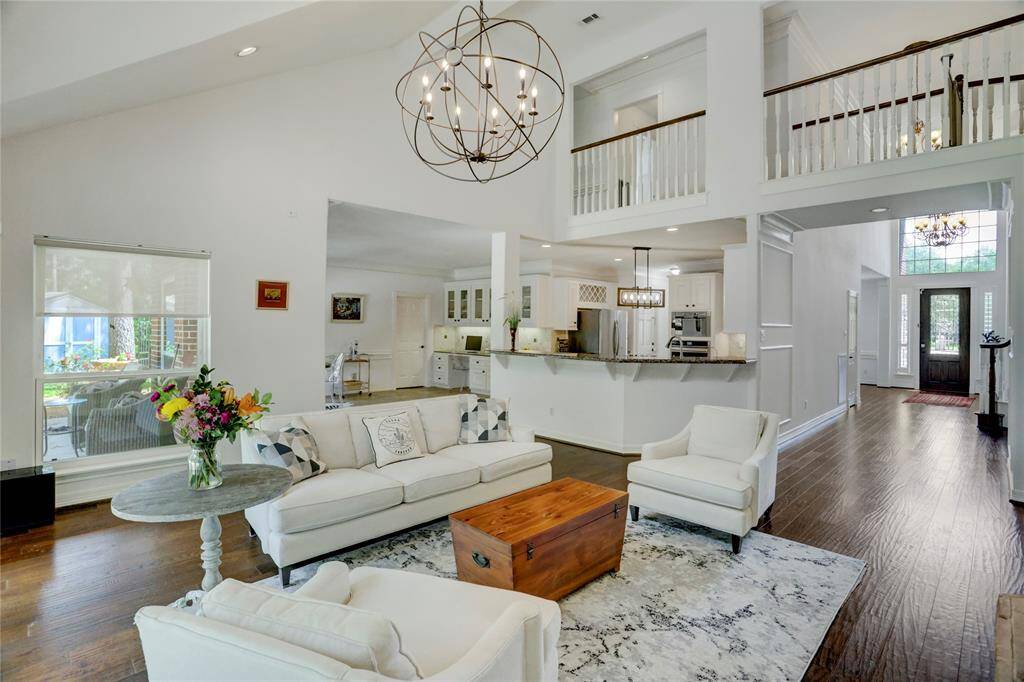 This spacious living area features an open floor plan with high ceilings, continuing the elegant, engineered wood flooring, and plenty of natural light. The room seamlessly connects to a modern kitchen with a breakfast bar and the large breakfast dining area while a stylish chandelier adds a touch of sophistication.