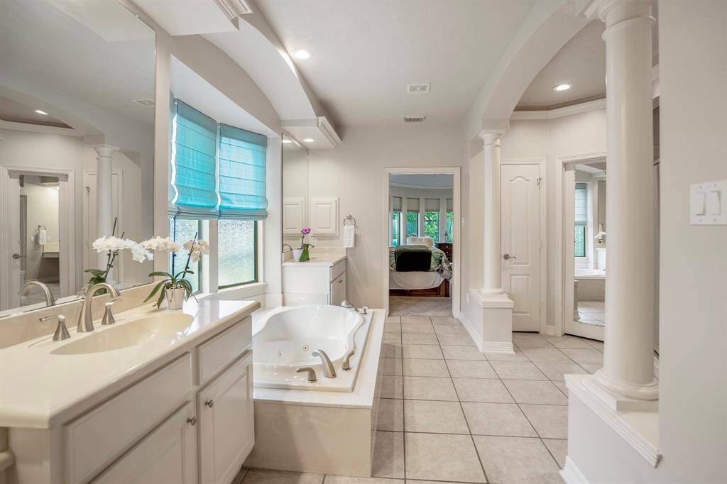 Dual sinks on opposite ends of the tub, tiled flooring, and as well as a separate shower with  dual shower heads and twin closets.