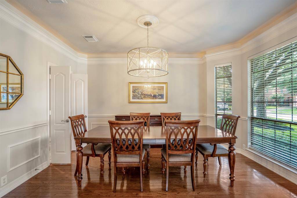 An elegant dining room features updated custom lighting, chair railings, crown molding and rich hardwood floors with an expansive wall of windows.
