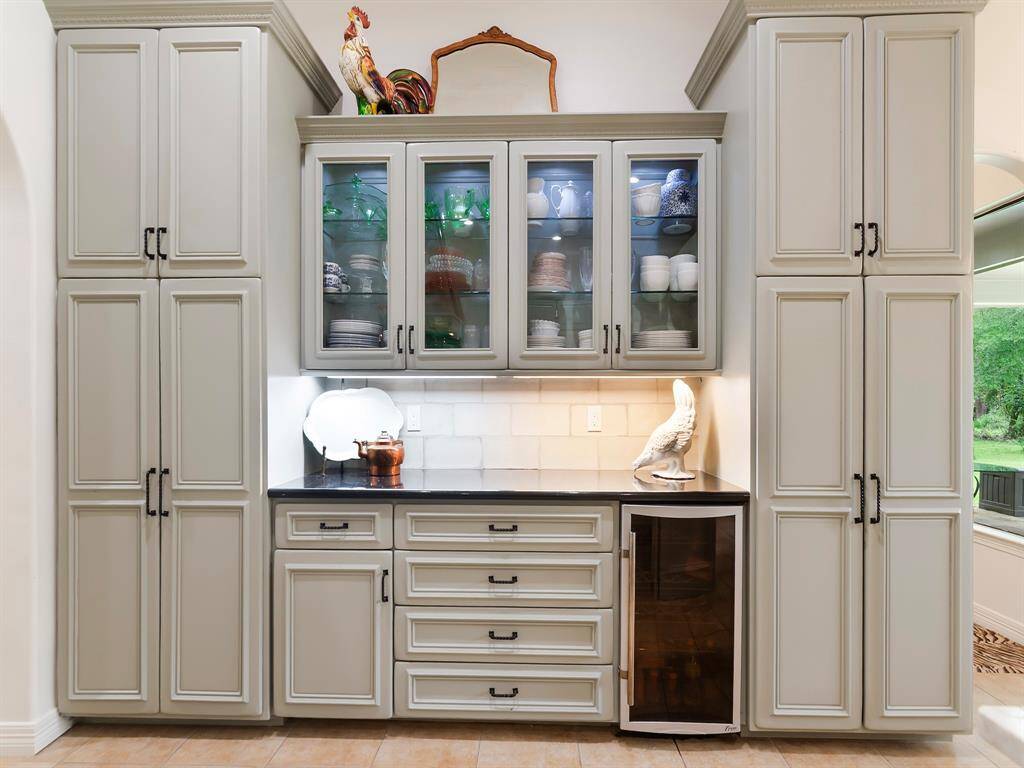 A kitchen wall of custom cabinetry offers beautifully organized storage for pantry items with a built-in countertop for housing a beverage cooler, drawers and closed storage below. Glass-front upper cabinets with glass shelves and soft under cabinet lighting add a touch of elegance perfect for displaying serveware.