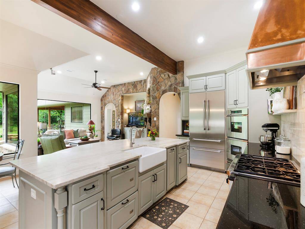 From this angle the farmhouse sink takes center stage beneath the warm wood beam ceiling, highlighting the kitchen's open friendly space.