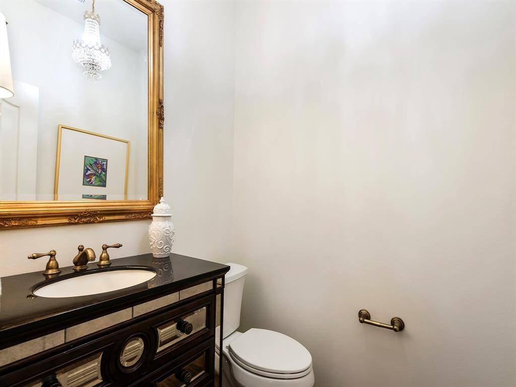 This elegant bathroom features a stylish vanity with brass fixtures, a large ornate mirror, and a classic chandelier, offering a touch of luxury.