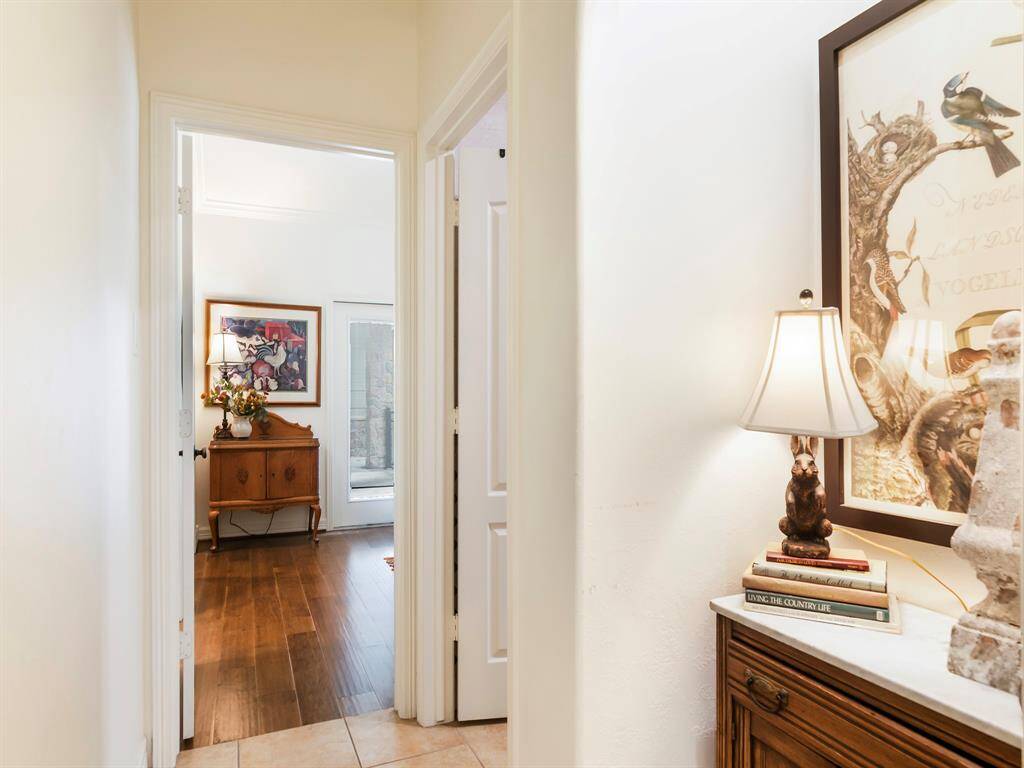 This photo showcases a bright hallway with tiled flooring leading to a secondary bedroom with warm wooden floors.