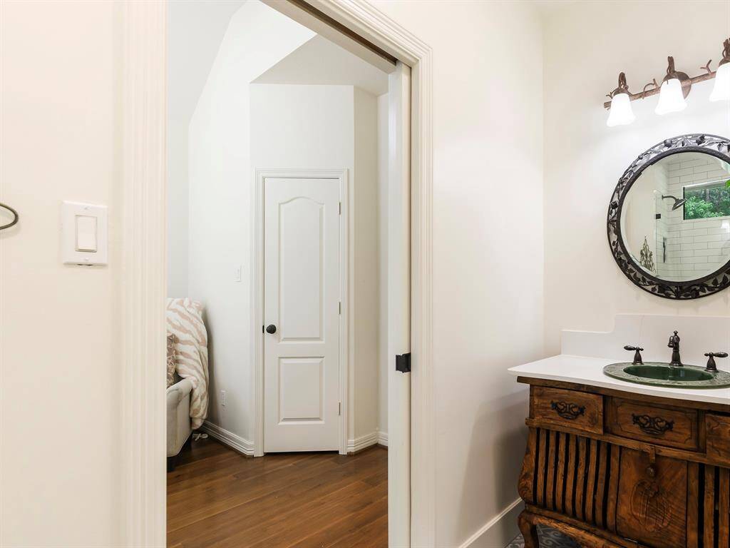 This photo showcases a bathroom with a vintage-style wooden vanity, a decorative round mirror, and elegant lighting. The room has white walls and hardwood floors.