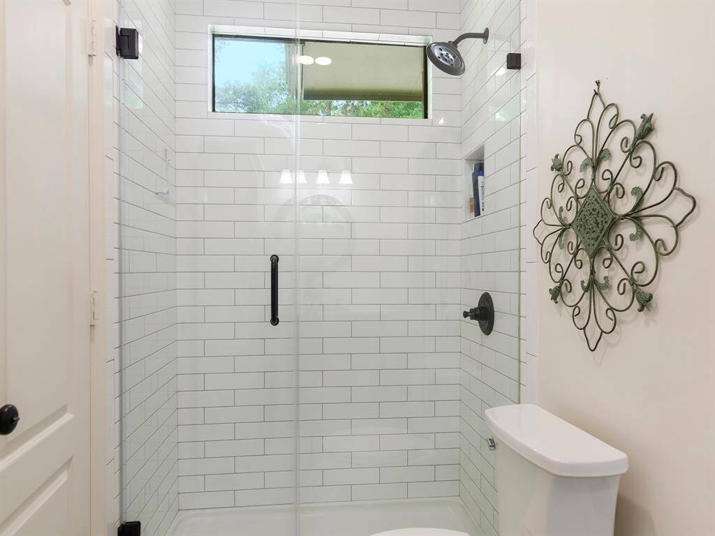 Modern bathroom with a sleek glass-enclosed shower and white subway tile. Natural light enters through an upper window, creating a bright and inviting space.
