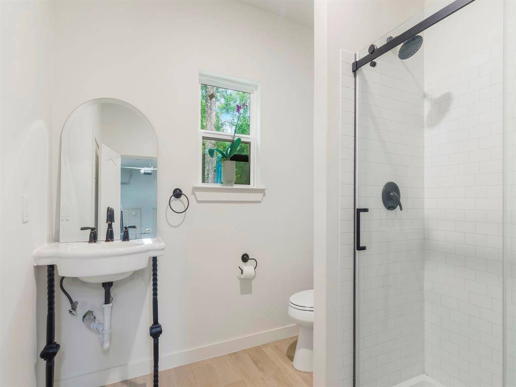 The workshop has access to this beautiful bathroom featuring a clean, modern design with a glass-enclosed shower, a pedestal sink with black fixtures, and a small window for natural light. The space is bright and minimalistic, with light color flooring complementing the white walls.