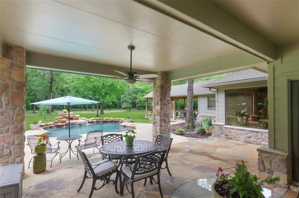 The backyard features a spacious covered patio with flagstone decking and stone-accented pillars, creating a natural and inviting outdoor retreat.