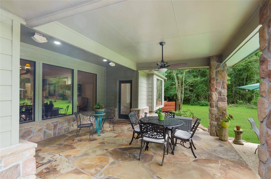 This photo showcases a spacious, covered patio with elegant stone flooring and walls. It features a ceiling fan and a view of a lush, green backyard, perfect for relaxation and entertaining.