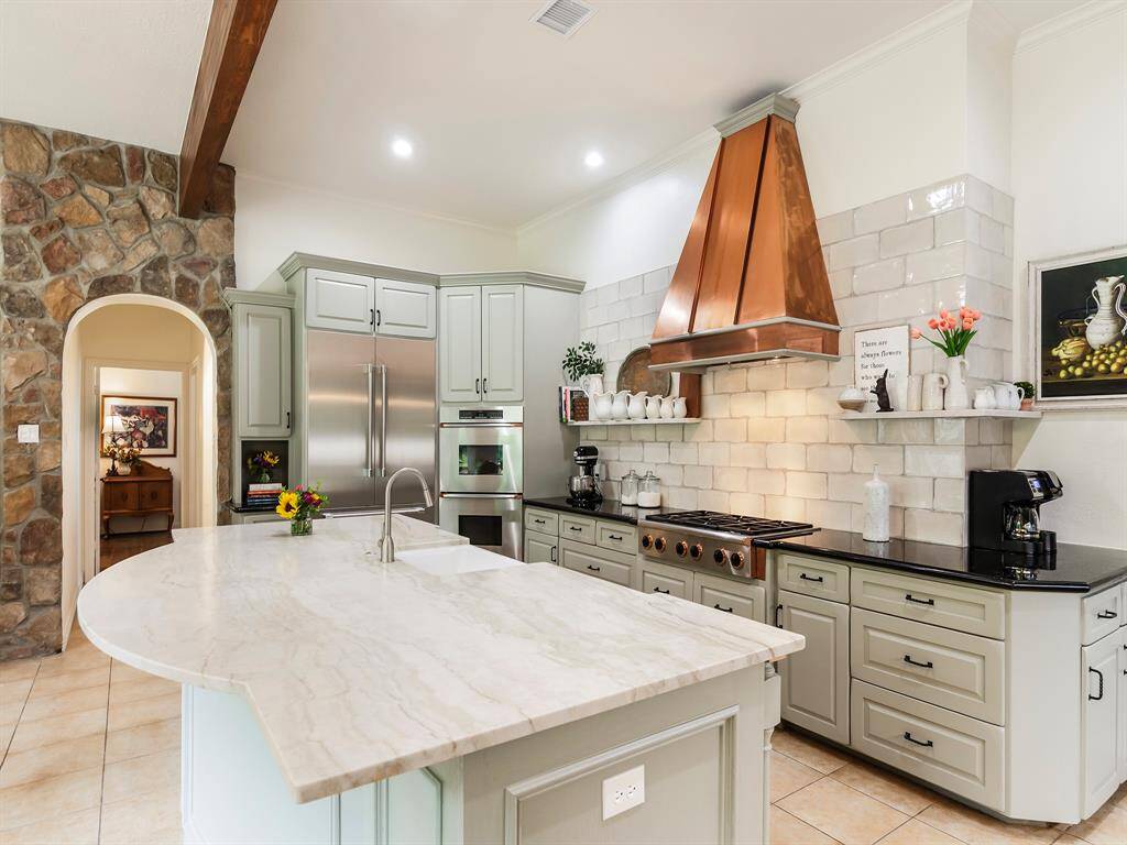 A striking copper-toned vent hood crowns the professional gas cooktop, flanked by double convection ovens and a warming drawer for effortless entertaining.
