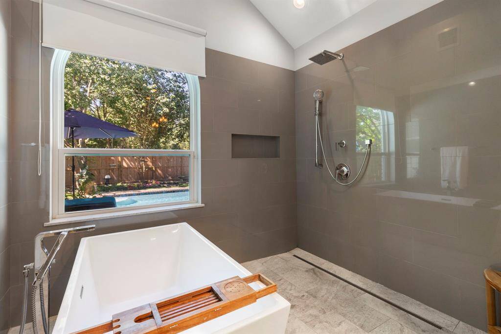 The focal point of the space is the sleek, modern freestanding soaking tub, in a doorless wet room with a tile surround, a storage niche, and updated tile flooring. A large walk-in closet completes the suite (not pictured), offering ample storage for every wardrobe need.