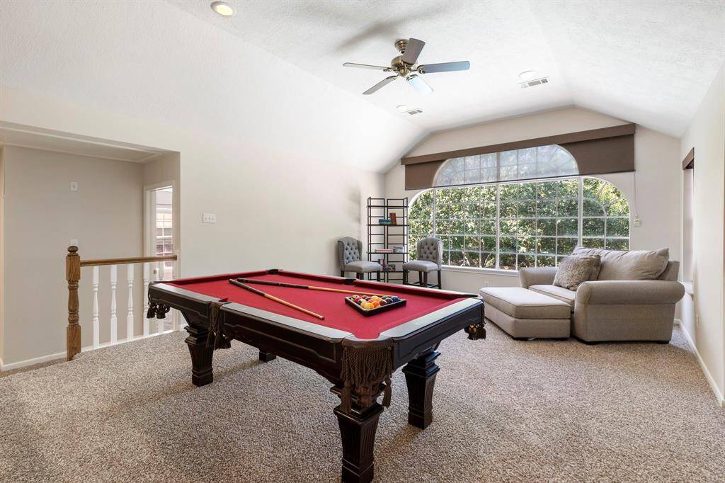 Upstairs, you'll find a spacious step-up game room with a vaulted ceiling that adds character and dimension. A stunning wall of windows offers panoramic views of the pool below, enhanced by custom shades for added comfort and privacy. The room comes fully equipped with a pool table and accessories, which will convey with the home, making it move-in ready for game night