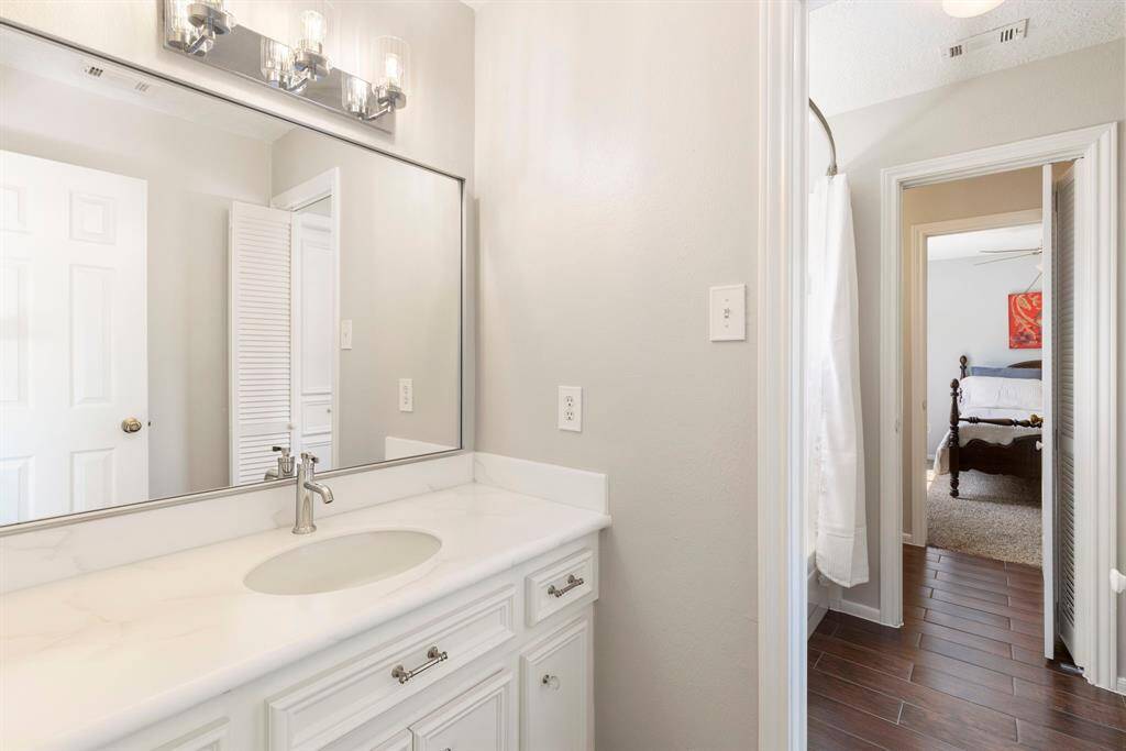 The shared wet area includes a tub/shower combo with a classic white tile surround and warm wood-look tile flooring, plus convenient linen storage.