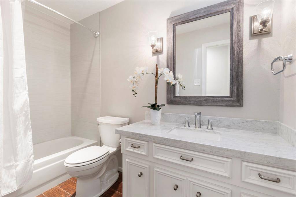 A full bath has sleek Carrara marble counters, white cabinetry, a decorative mirror stylish sconce lighting and a tub/shower combo with a tasteful tile surround.  This beautifully remodeled bathroom is filled with natural light, thanks to a well-placed skylight!