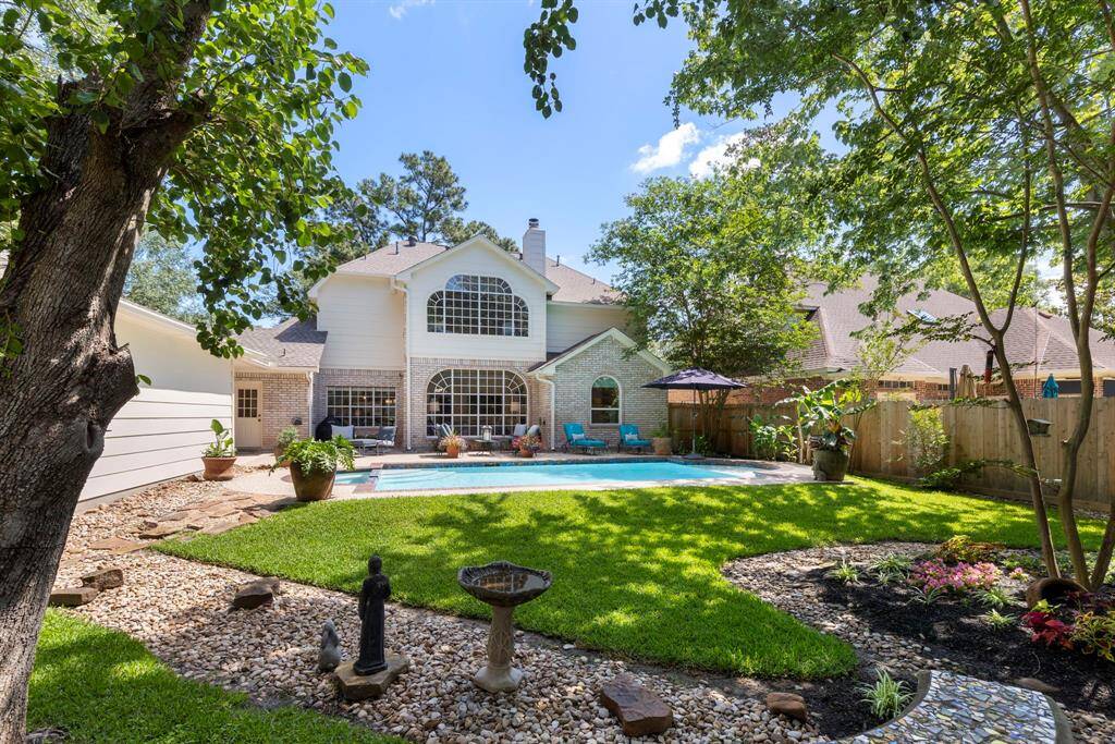 Surrounding the pool, you'll find lush green grass, a charming flagstone pathway, and a mix of rock and mulch flower beds filled with vibrant plants.