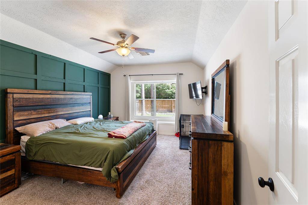 This inviting living room features a cozy fireplace, and a ceiling fan. It has a spacious layout for  comfortable seating, a mount for TV, and large windows for natural light. The open entrance and staircase add a welcoming touch.