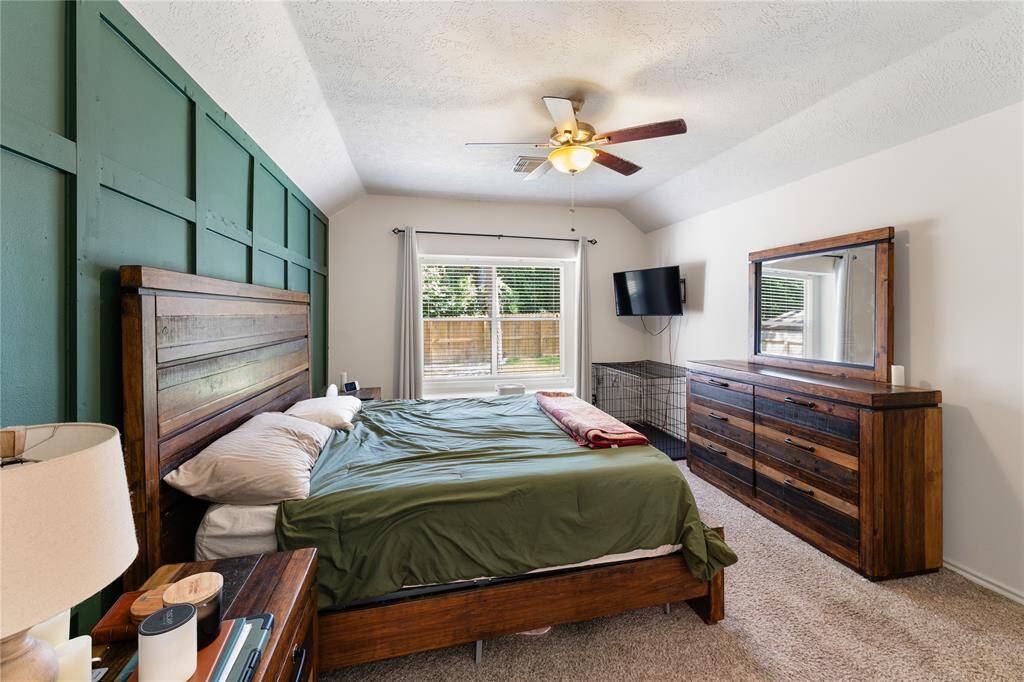 This spacious living room features a cozy fireplace, large windows with ample natural light, and an open layout connecting to the dining area and kitchen. The room is accented with a ceiling fan, and space for furnishings, creating a warm and inviting atmosphere.