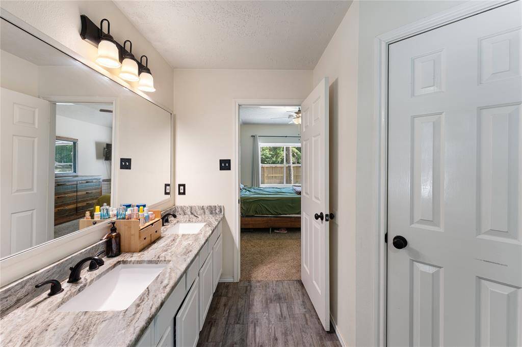 This inviting bedroom features a large wooden bed with a matching dresser, a deep green accent wall, and a ceiling fan. It leads to a bright en-suite bathroom, adding convenience and style.