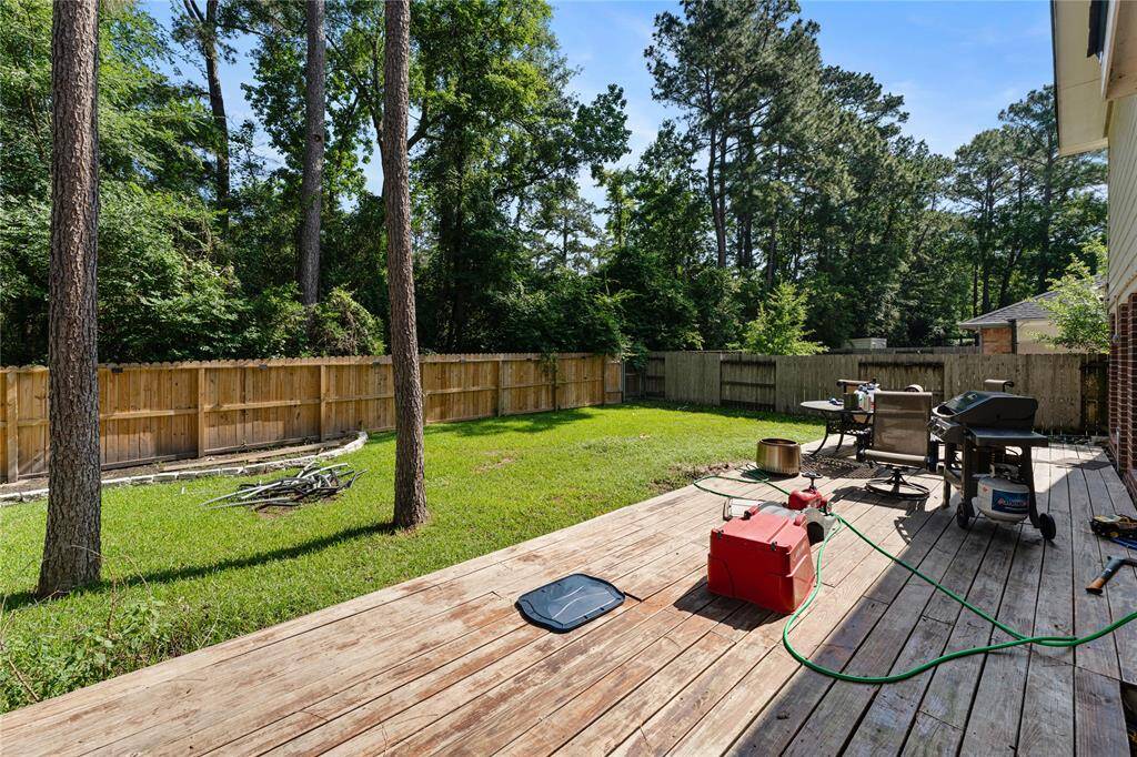 Spacious backyard with lush grass, mature trees, and a wooden fence for privacy. Features a small garden area with a stone border, a deck for outdoor seating, and a storage shed. Ideal for family activities and entertaining.