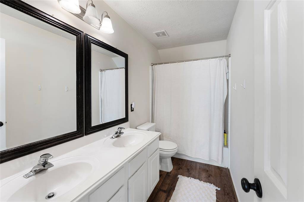 A spacious backyard with a wooden deck, perfect for outdoor entertaining. The yard is enclosed by a wooden fence and surrounded by tall trees, providing privacy and a serene atmosphere. A grill and patio furniture suggest a great spot for gatherings.