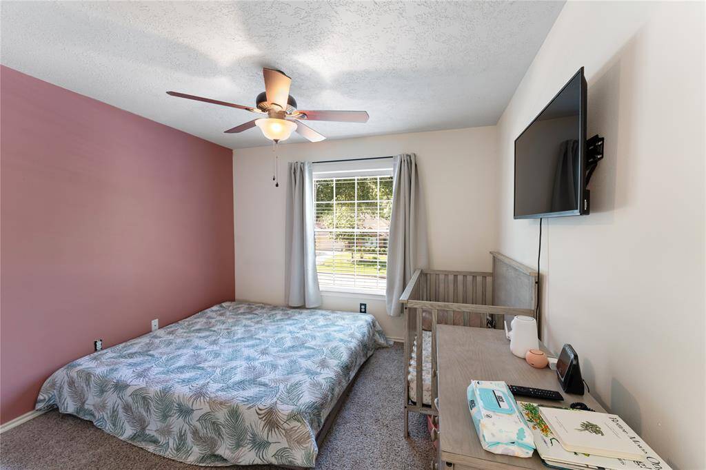 This room features neutral walls, carpeted flooring, and a ceiling fan with a light fixture. It includes a window with blinds, offering natural light. Currently, there is minimal furniture, including a small table and bed frame parts, providing a versatile space for customization.